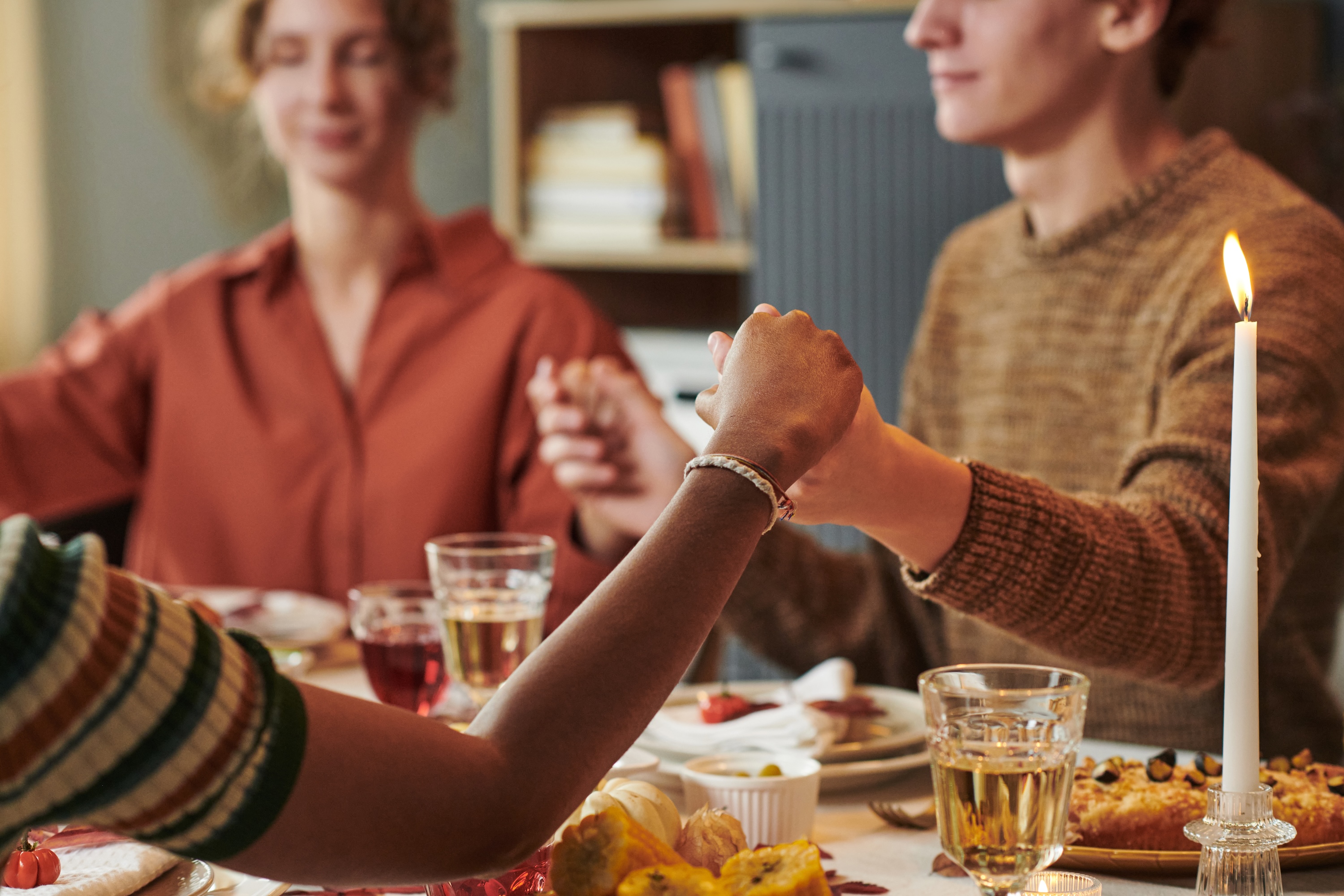 Multi-ethnic young adults holding hands around a table