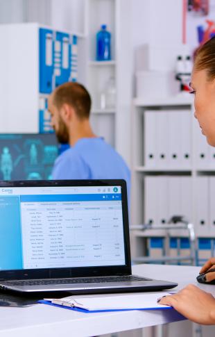 a woman in scrubs checking information on a laptop